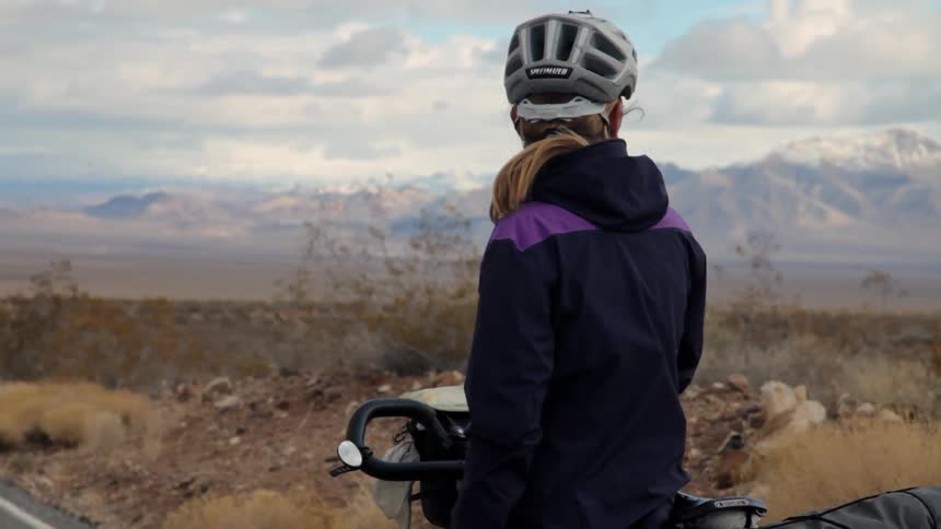 A woman is standing by her bike taking in a view of the mountains