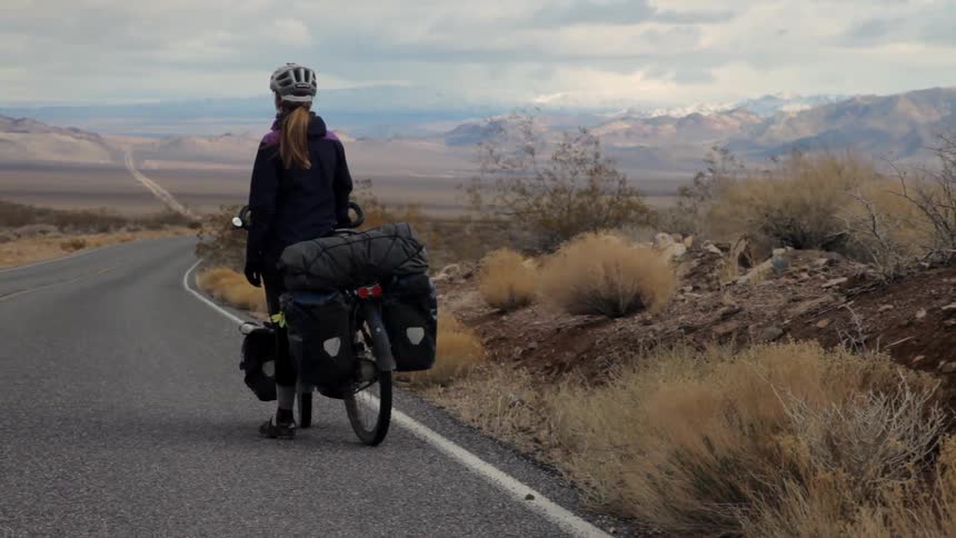 Woman on a bike stands on the side of the road looking out