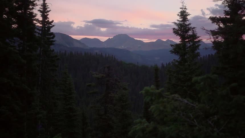 The sun sets over mountains and pine trees