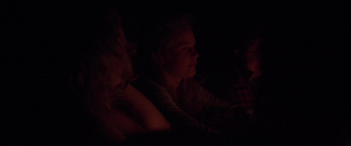 Women talk and brush back their hair as they sit at a campfire at night