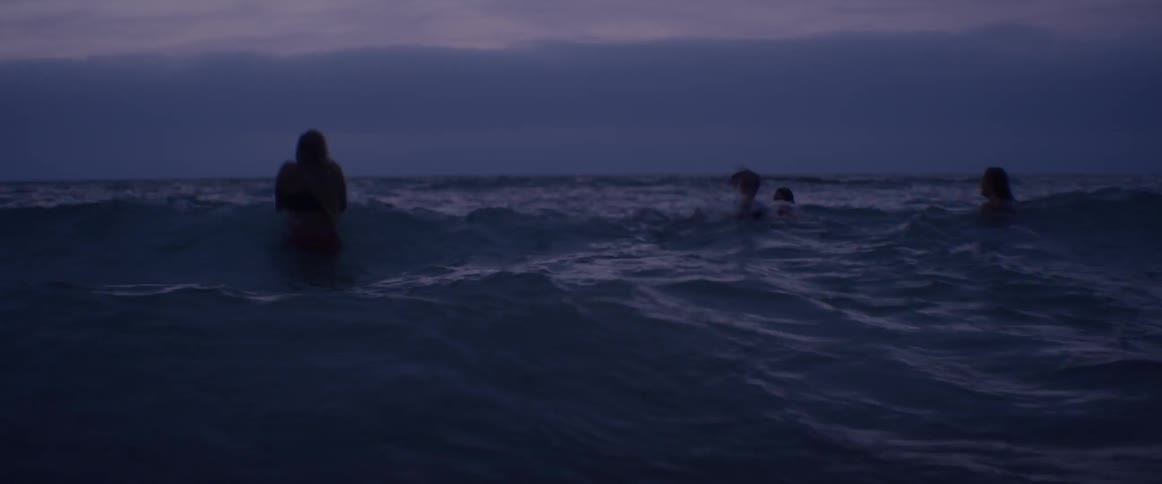 People swim in the ocean at sunset