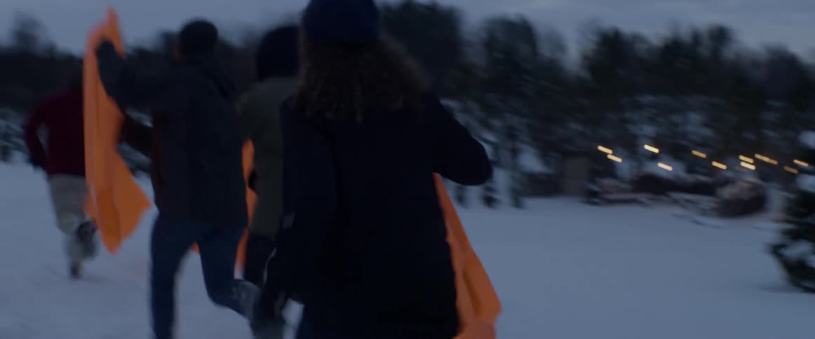 A group of people are running in the snow with some orange sleds
