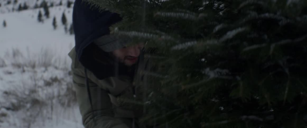 A man is cutting down a tree as it snows