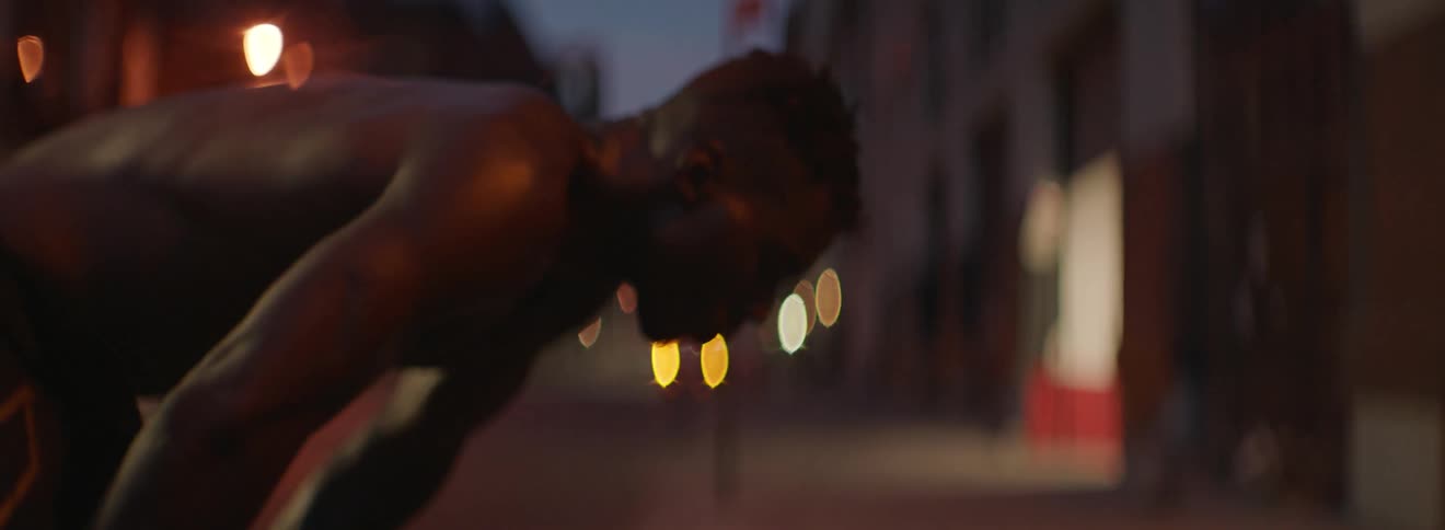 Shirtless man bends over and looks at a building