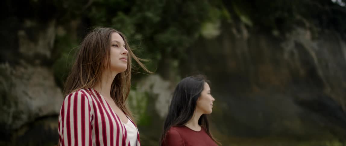 Two women stand outside with trees and rocks in the background