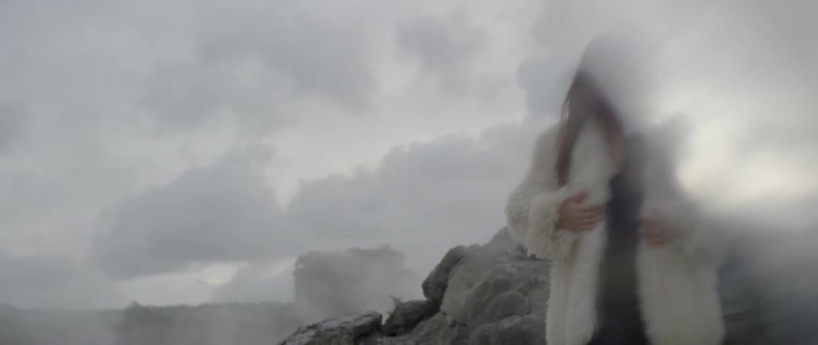 A woman wears a fur coat outside on a cloudy day