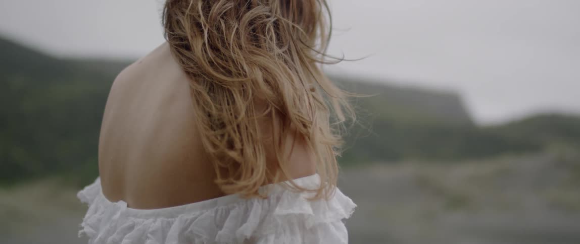 A woman's hair blows in the wind near the beach