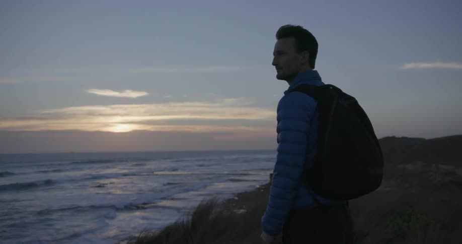 A man stands overlooking an ocean at sunset
