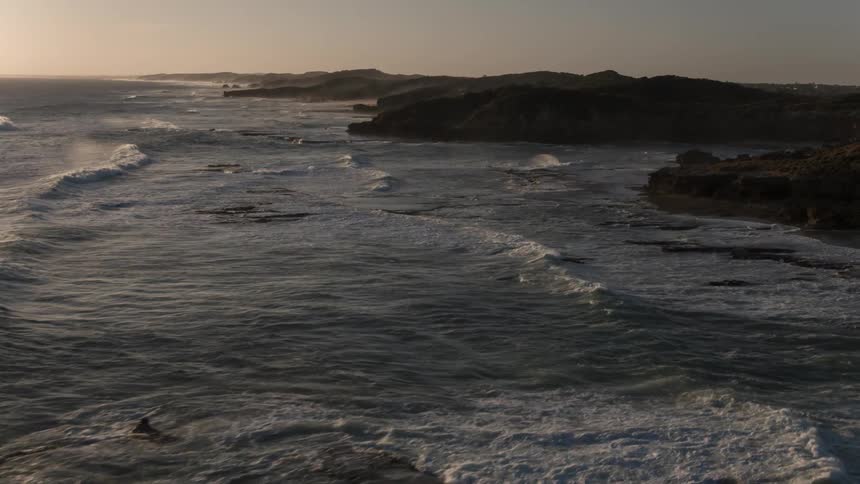 The water is rough waves hitting the rocks of the shore