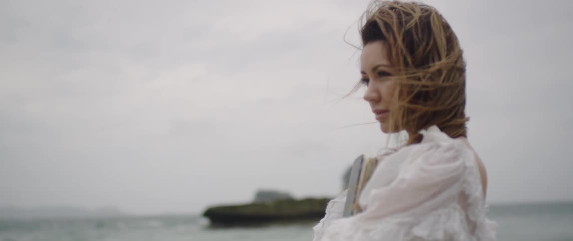 Woman clasps a large black binder and stands by the ocean