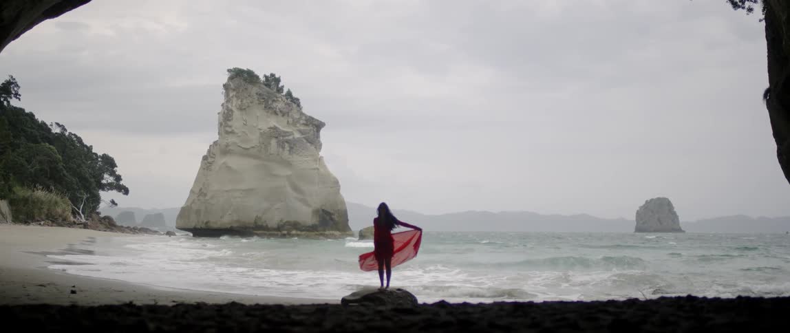 Woman stands near the ocean waving her long skirt
