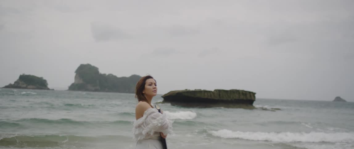 Woman clasps a large black binder and stands by the ocean