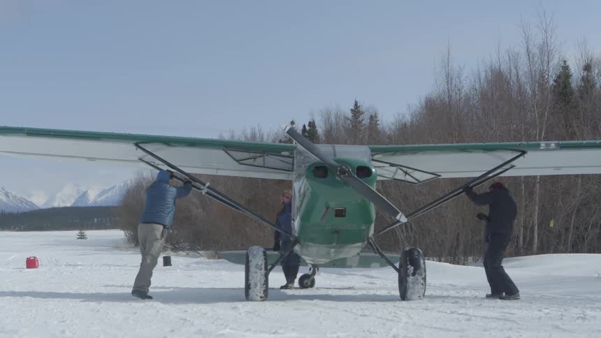 Three men pushing a small airplane on a snowy ground