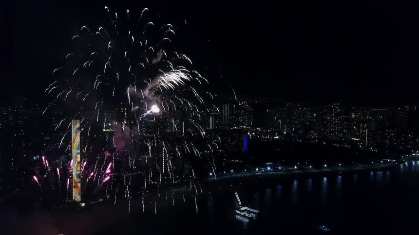 Fireworks shooting off over bay near large city at night