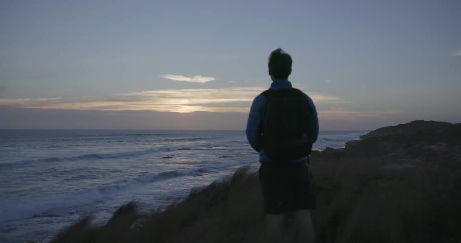 A hiker stops to look at the ocean view at sunset