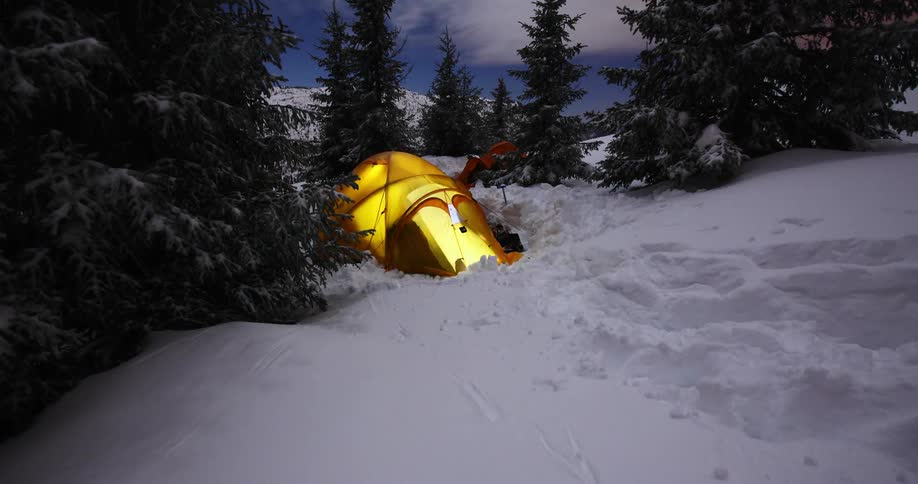 A person moves in and around a tent in a snowy clearing
