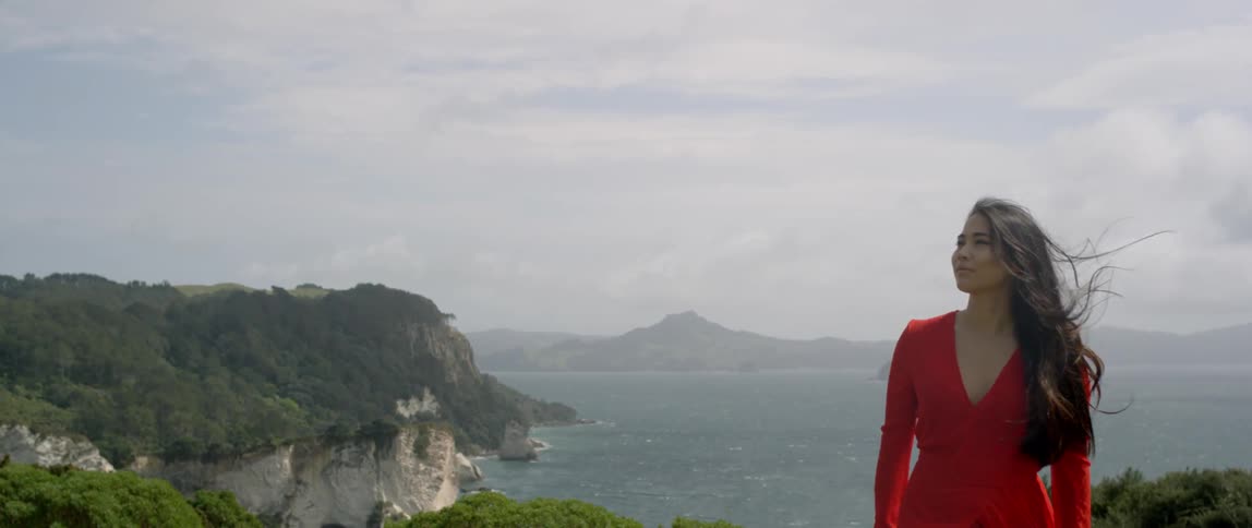 Woman stands atop a cliff by the ocean
