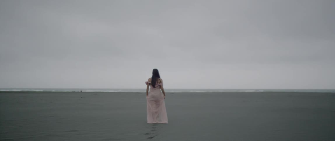A woman walks through the sand wearing a pink dress