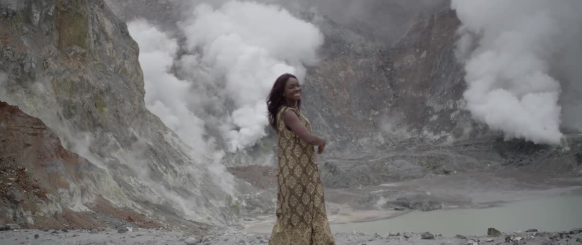 A woman waves her arms happily while steams rises from the ground behind her