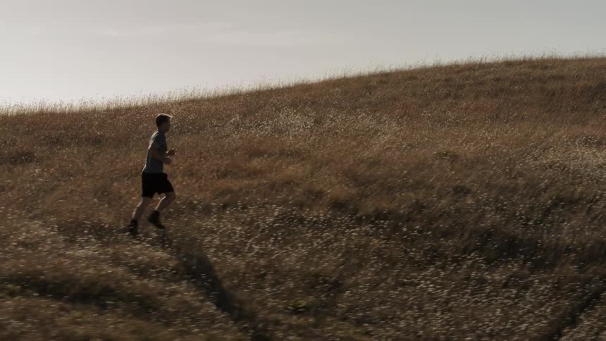 A man jogs across a grassy hill
