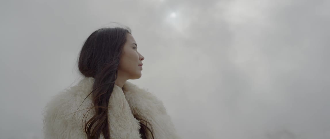A woman wearing white stands under a cloudy sky