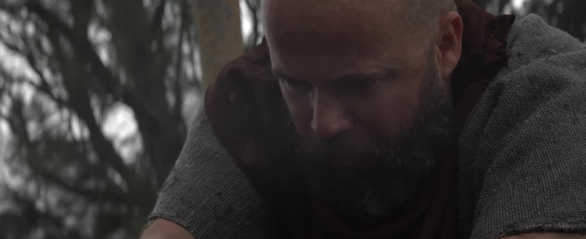 A bearded man eats outside