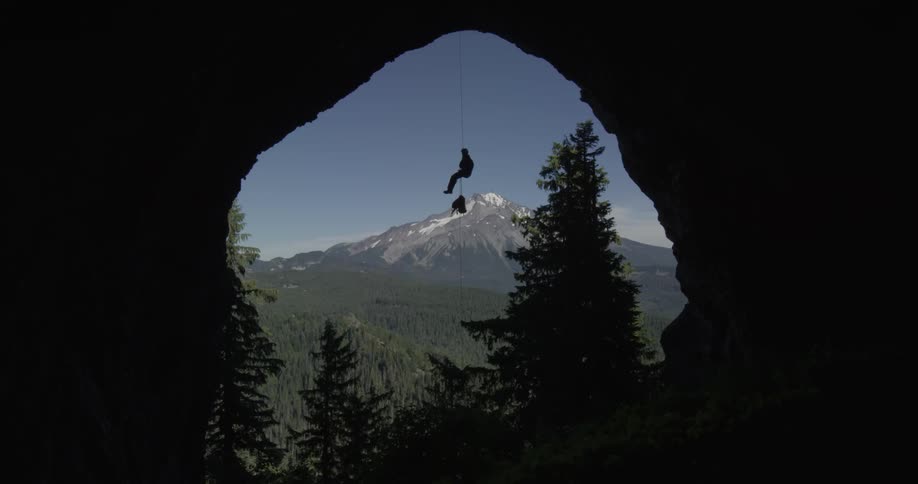 Man dangling from a rope at the opening to a huge cave