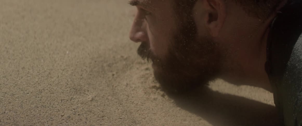 A shipwrecked man lies face first in the sand
