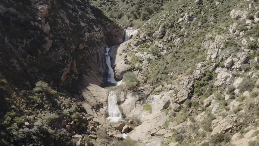 A waterfall in a ravine lined with rocks and small bushes