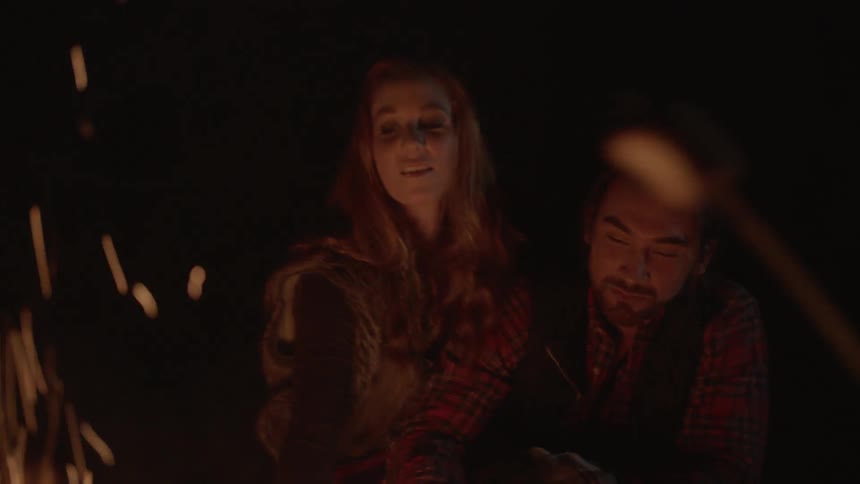 A couple is laughing at a campfire