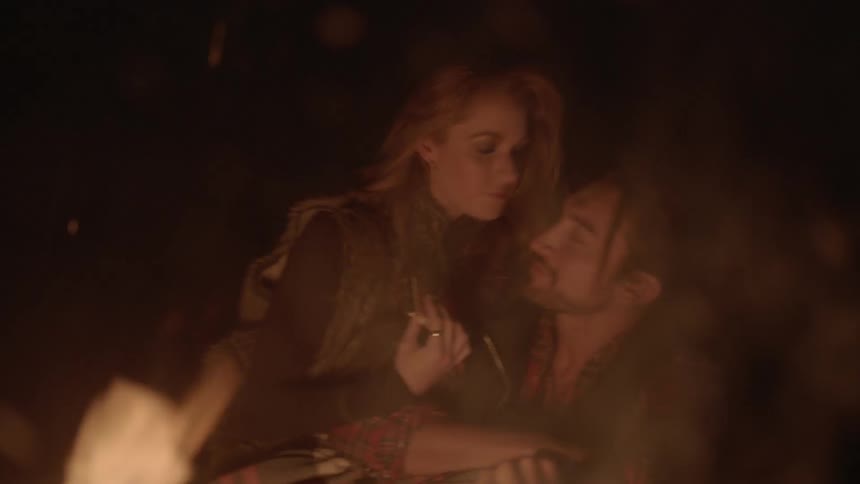Man and woman cuddling and kissing in front of a fire