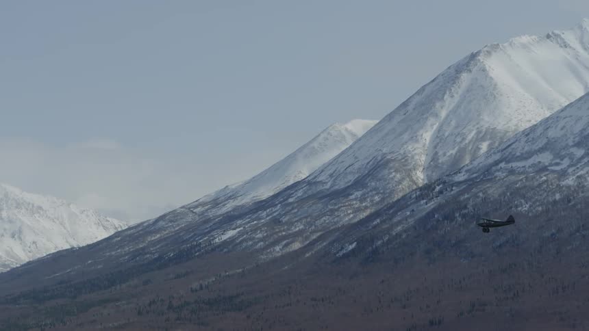 Small airplane flying with snowy mountain in background