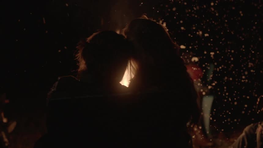 People hug near a fire at night