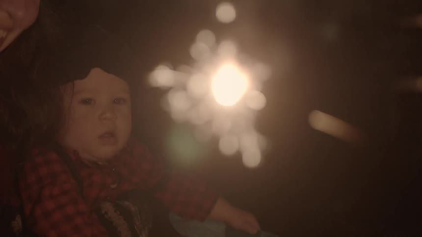 Woman with a child holding a sparkler outside at night
