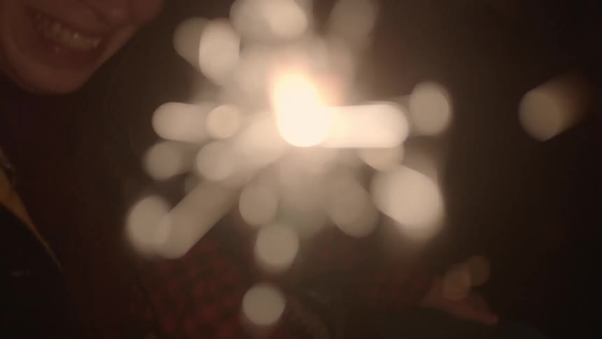 Woman holding a child and a sparkler outside at night