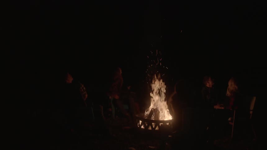 Four people sitting by a campfire lighting off fireworks