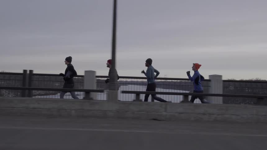 People jog together in a row over the bridge