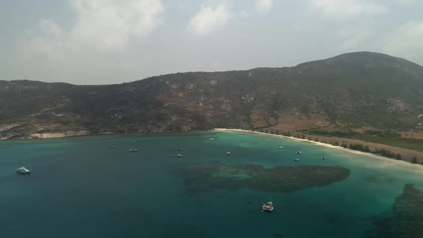 A crystal clear sea with several boats on it is surrounded by a mountain