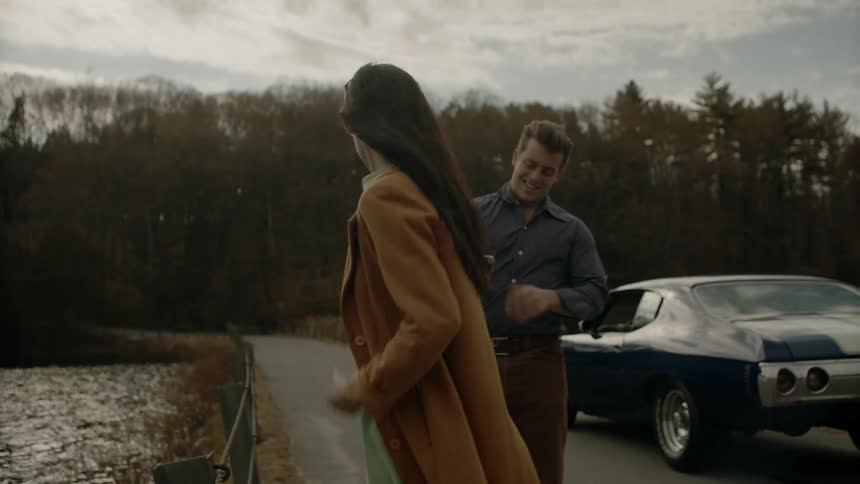 A man takes a picture of a woman standing on the road