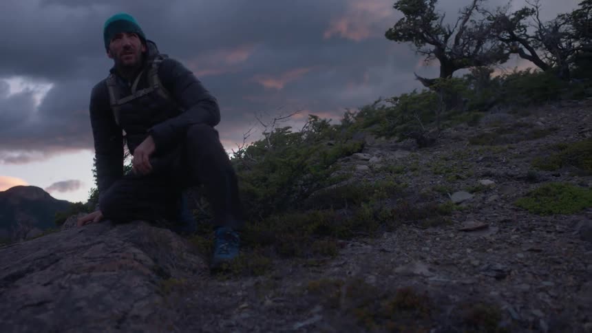 A man sits on the rocks looking below