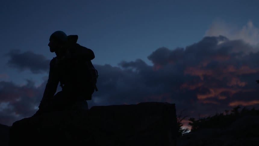 A man is sitting on the edge of a rock at dusk