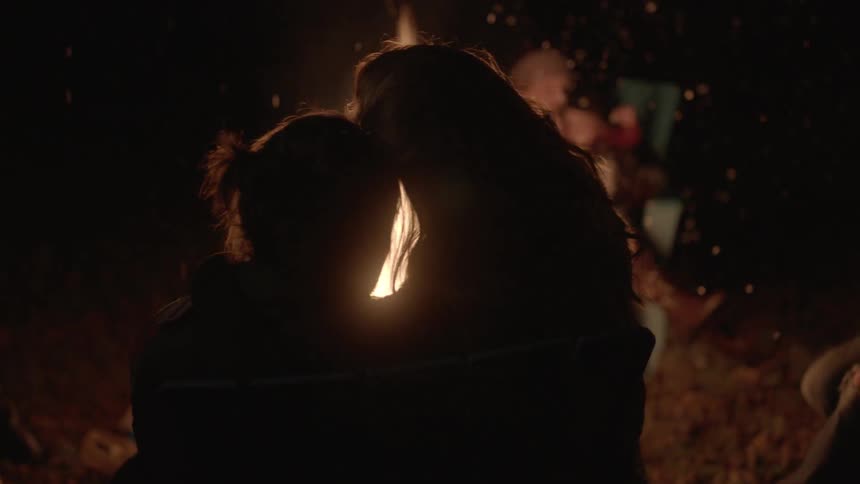 People cuddle next to a campfire