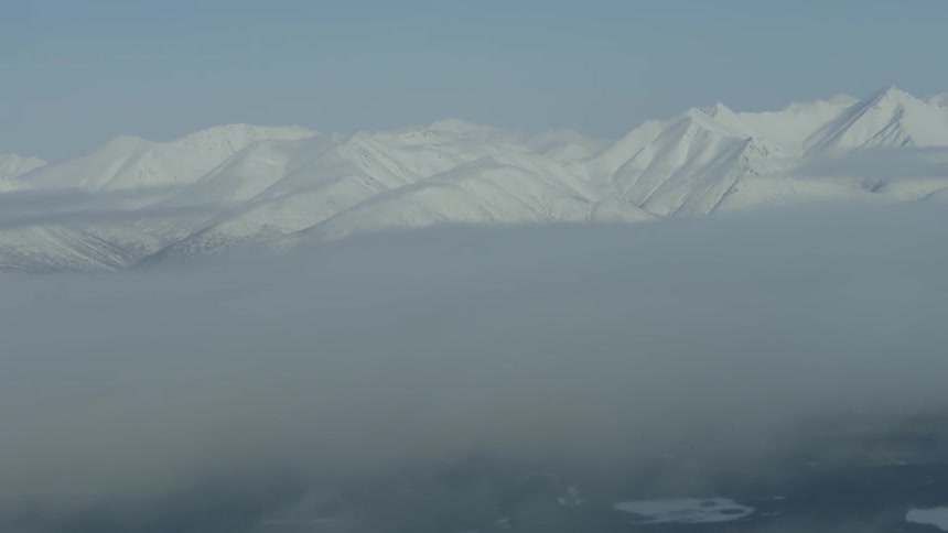 A mountain range is completely covered in snow as fog settles below