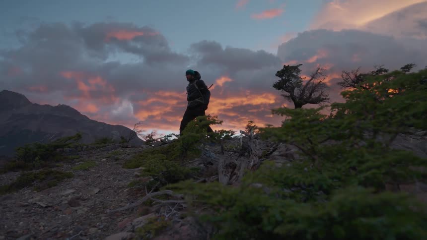 A man walks down a windy hill at sunset