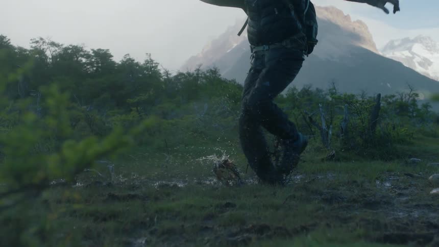 A man hikes through the marsh and splashes in a puddle