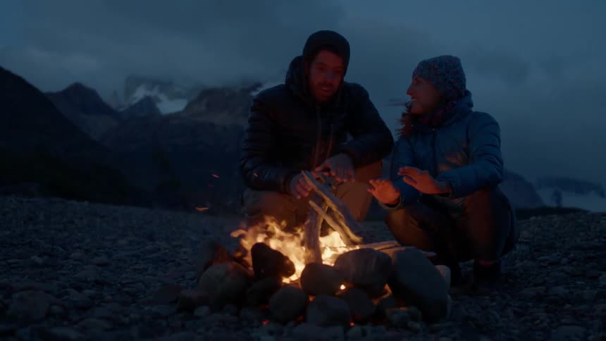 Two people sit around a campfire at dawn