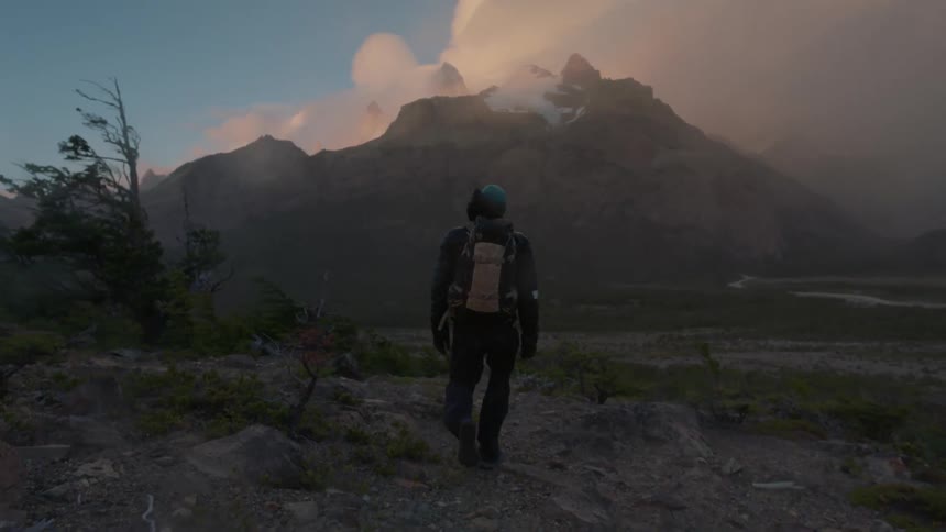 Man wearing a backpack walks towards a mountain