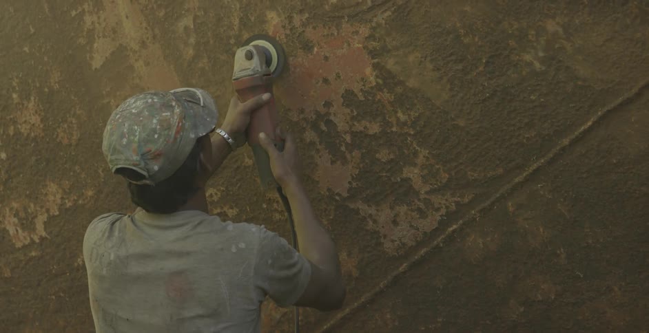 A man uses a sander on a metal barge
