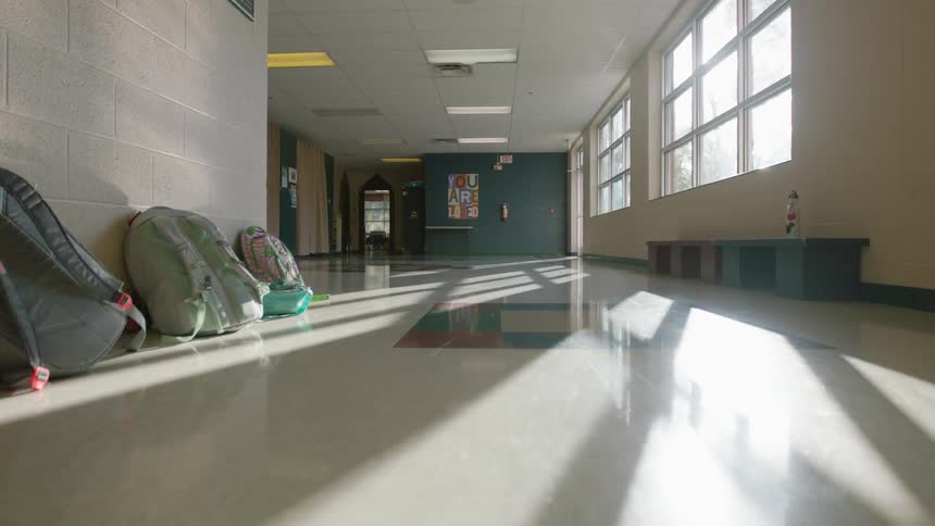 Backpacks sit stacked against a schoolhouse wall