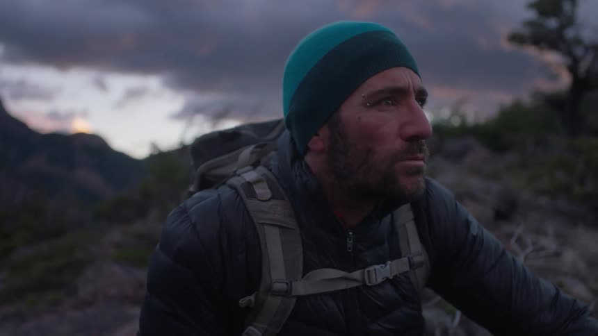 A man is crouching down on the mountain